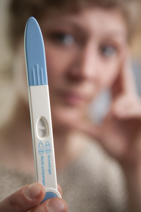 Foto mit Schwangerschafttest im Vordergrund und Frau im Hintergrund
