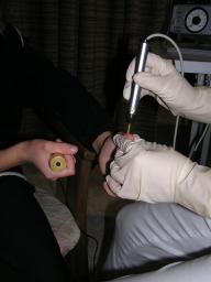 Foto einer Elektroakupunkturbehandlung, Heilpraktikerin hat Stift in der Hand, Patientin hält den Gegenpol