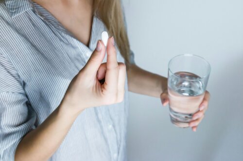 Eine Frau hält in der einen Hand eine Tablette und in der anderen Hand ein Glas Wasser